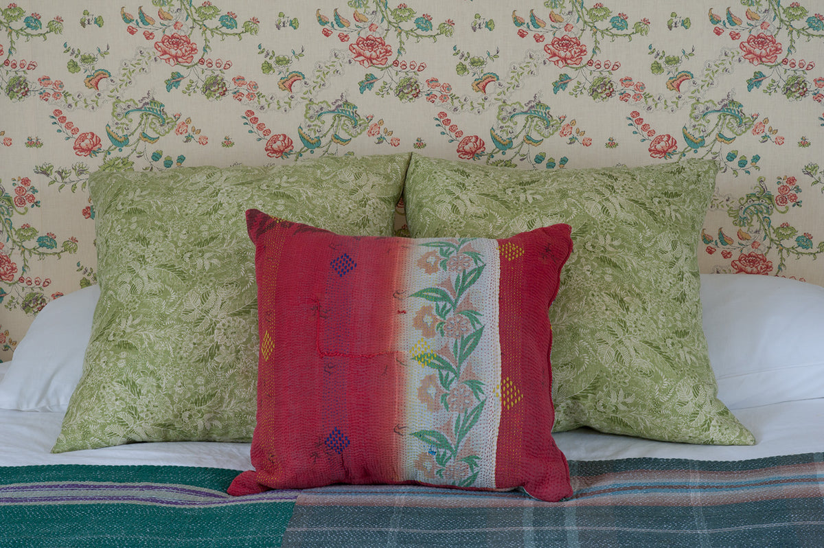 A decorative throw pillow in the center of a bed, styled with two large Wildflowers Green pillows, and a red floral accent pillow, set against a Bouquet Green headboard designed by Kathryn M. Ireland