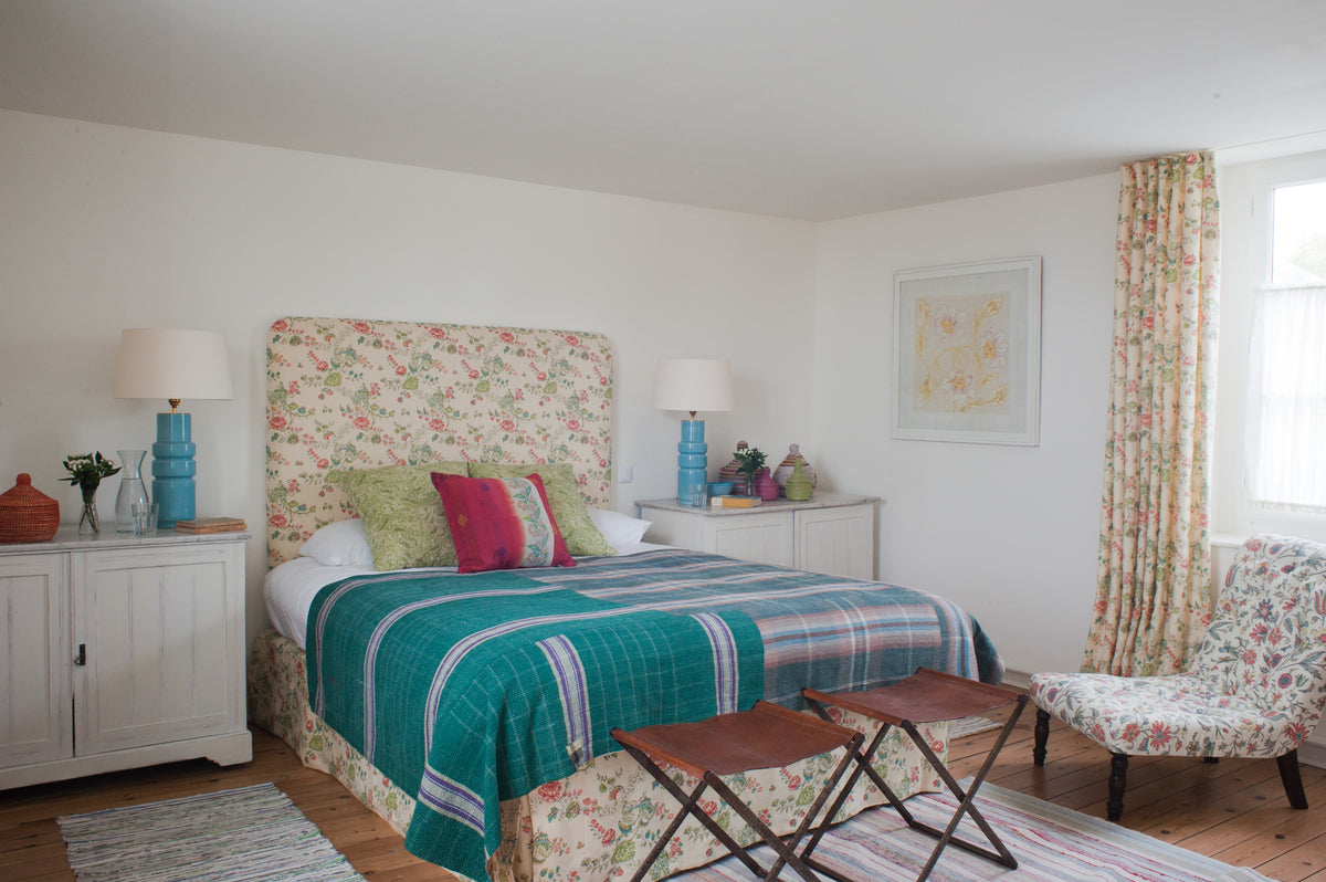 A cozy bedroom featuring a bed and curtains in Bouquet Green, pillows in Wildflowers Green, and a chair in Tatiana Red/Pink/Blue designed by Kathryn M. Ireland