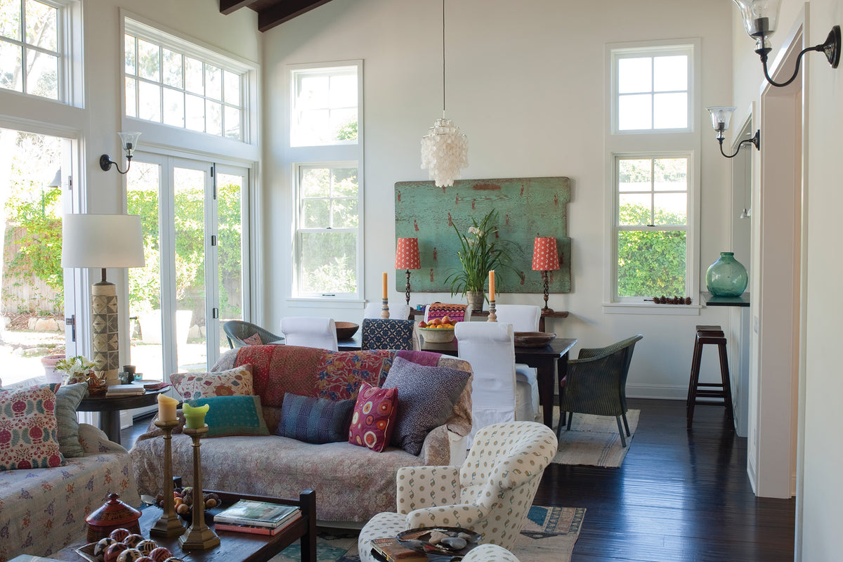A bright, modern living room featuring a patterned floral sofa with colorful throw pillows and a Casablanca Natural Natural/Sky & Mustard armchair designed by Kathryn M. Ireland