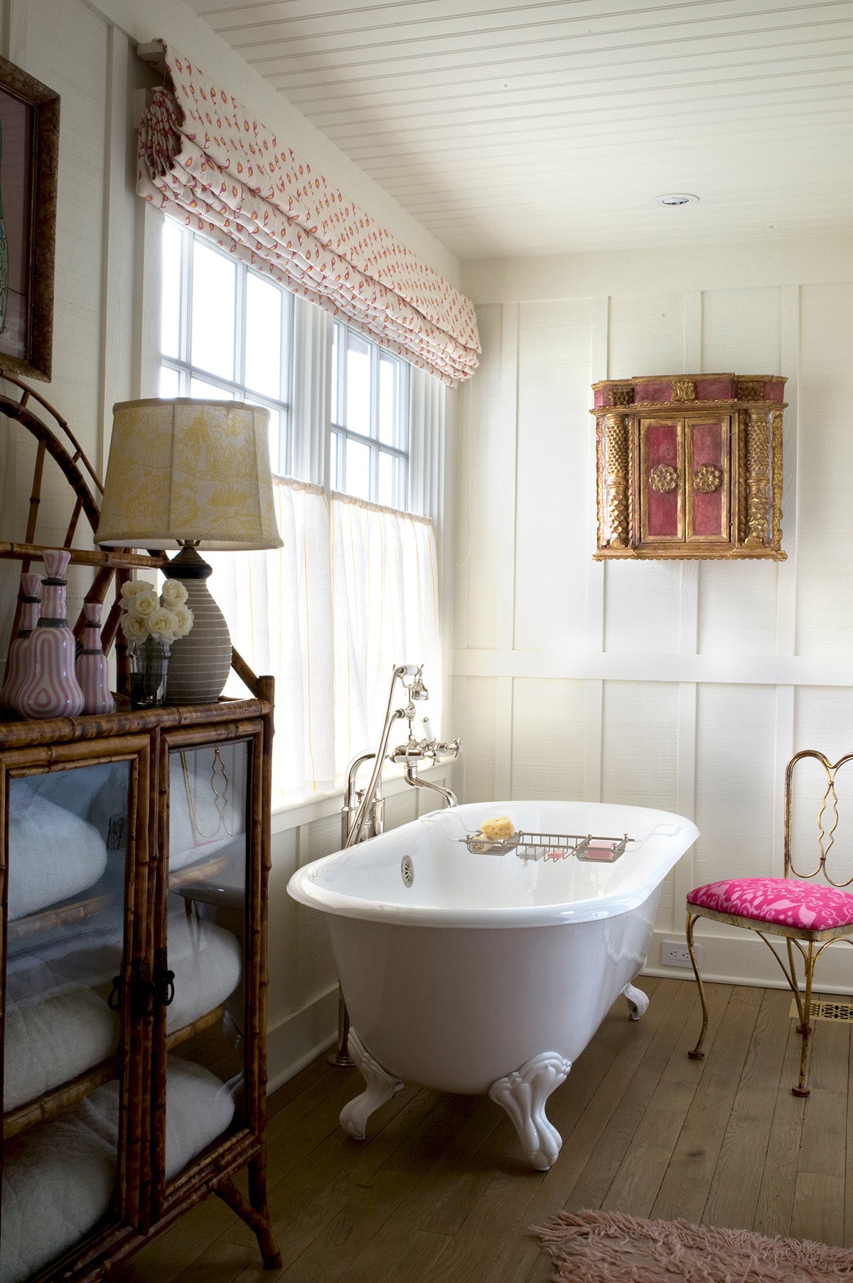 A vintage-style white clawfoot bathtub in a bright, paneled bathroom with a Casablanca Natural Natural/Flame & Mustard roman shade and Sheer Stripe Yellow curtains designed by Kathryn M. Ireland