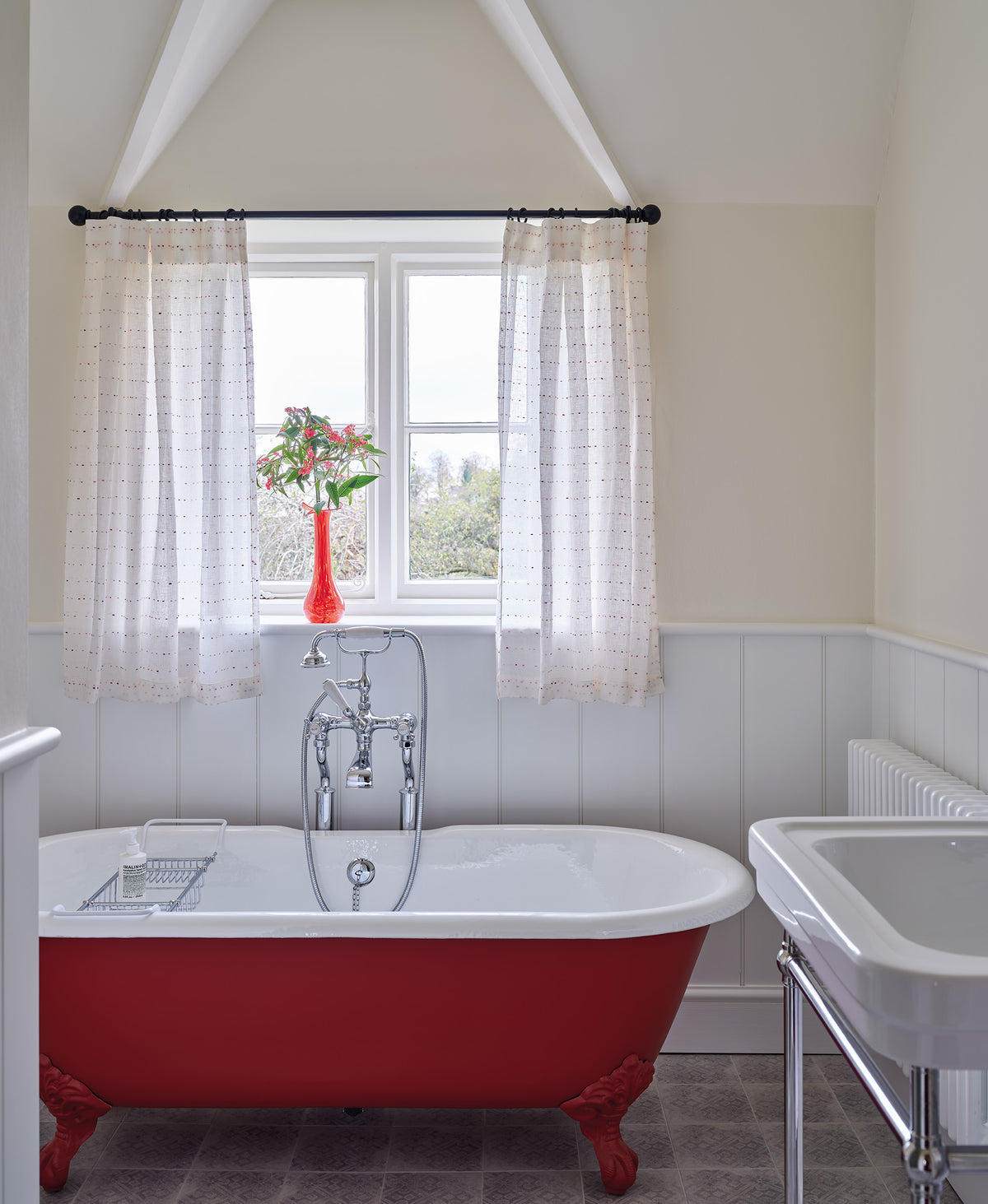 A classic red and white clawfoot bathtub in a bathroom in a Cotswolds home designed by Kathryn M. Ireland featuring Sheer Confetti Desert Rose curtains
