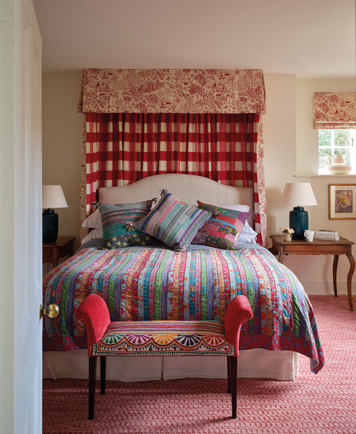 A bedroom in a Cotswolds home designed by Kathryn M. Ireland featuring a bed canopy and window covering in Toile Red and Ikat Check Red