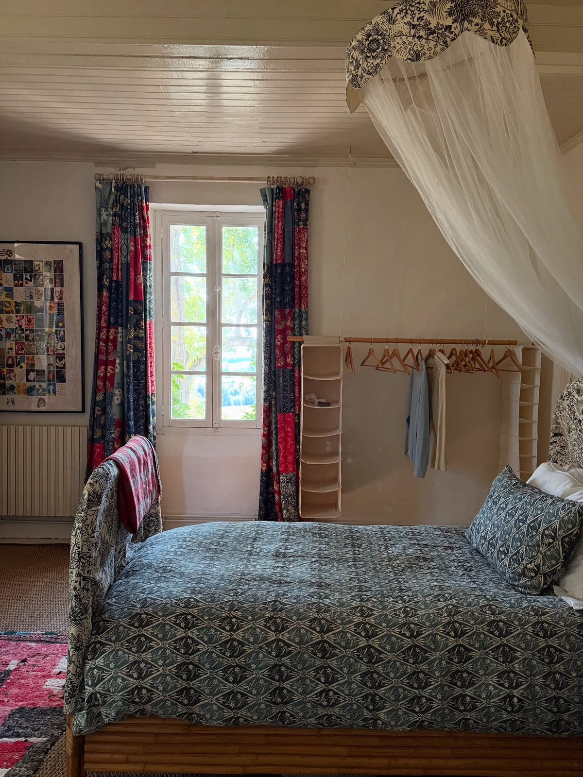 A cozy bedroom featuring a bed with Diamond Batik Indigo comforter and matching pillow, draped with a white sheer canopy with a cap and headboard in Toile Blue, designed by Kathryn M. Ireland.