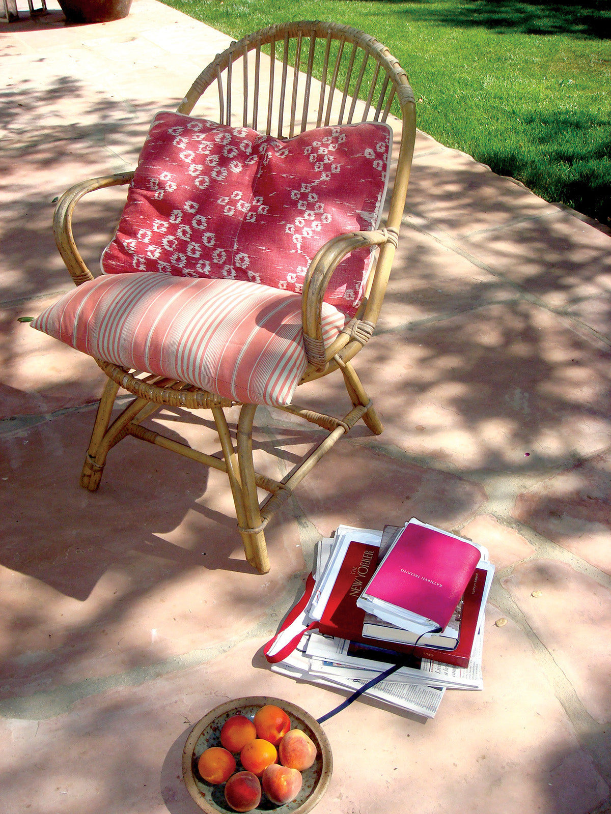 A rattan outdoor armchair with a Gitana Red pillow designed by Kathryn M. Ireland