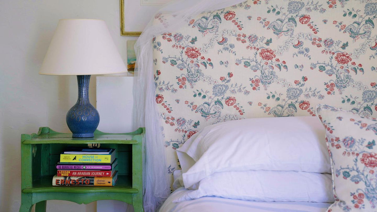 A close-up of a bed with a headboard in Bouquet Blue/Coral and matching pillowcases, designed by Kathryn M. Ireland.