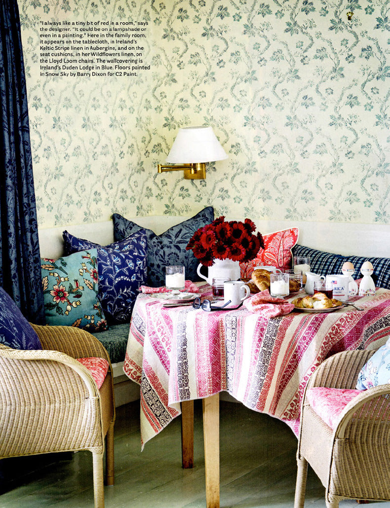 A page in House Beautiful magazine showing a dining nook in a Cape Cod home designed by Kathryn M. Ireland featuring a tablecloth in Keltic Stripe Aubergine and Froxfield Indigo wallpaper.
