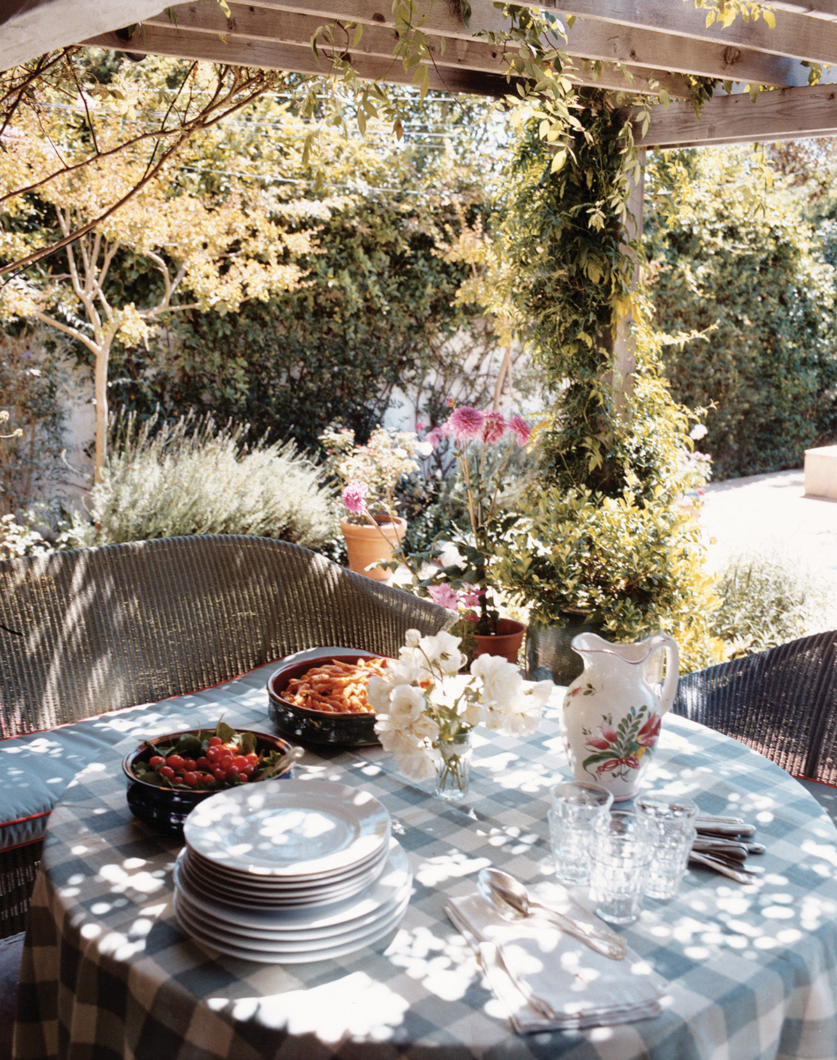 A round outdoor dining table set under a wooden pergola with a Ikat Check Blue tablecloth designed by Kathryn M. Ireland