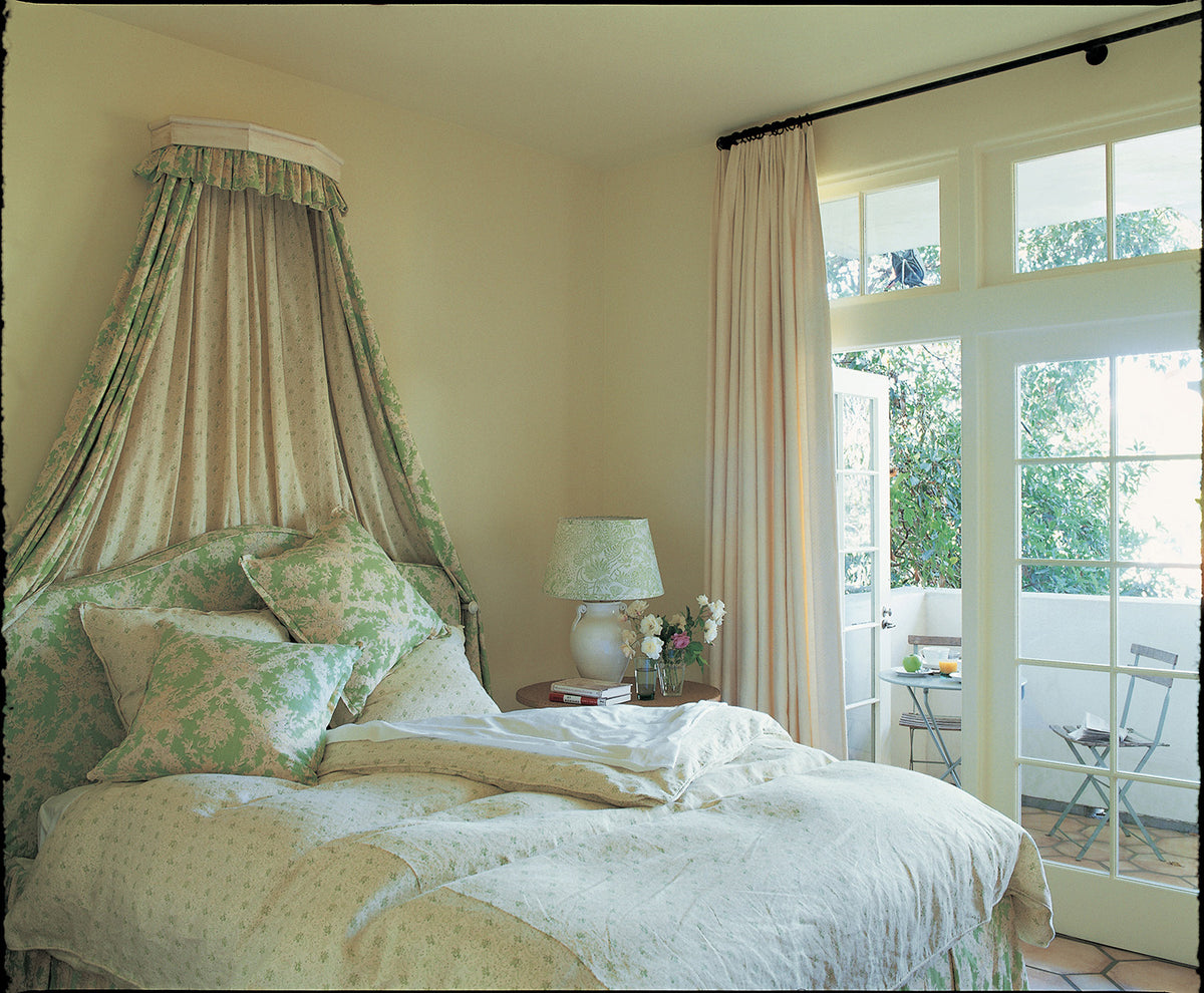 A classic French-chic bedroom featuring a tall fabric canopy bed with Ikat Green and Floral Green curtains, bedding, and pillows designed by Kathryn M. Ireland