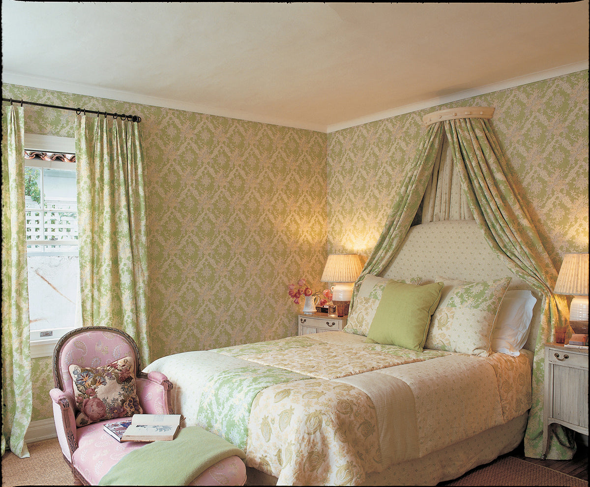 A beautifully styled bedroom featuring a bed with an Ikat Green canopy and curtains, a Floral Green headboard, a quilt of various Kathryn M. Ireland fabrics, and Ikat Green wallpaper designed by Kathryn M. Ireland