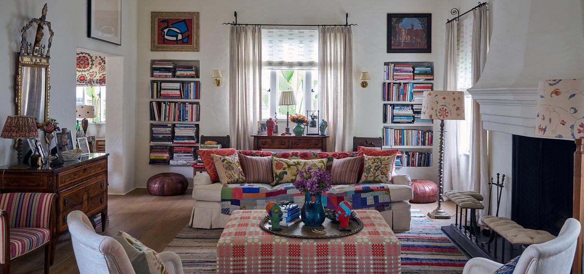 A living room designed by Kathryn M. Ireland featuring Kippford Stripe Multi pillows, Bukhara Suzani Multi on Oatmeal lampshades, Ottoman Stripe Royal Multi armchair, and Sultan Suzani Orange window treatments.