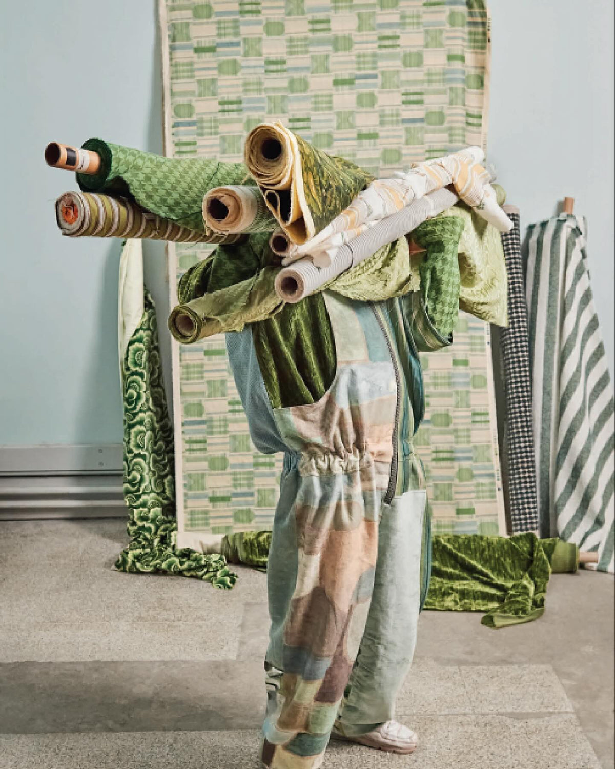 A page from World of Interiors magazine featuring a person holding a number of rolls of fabric with Kathryn M. Ireland's Kantha Sea fabric hanging in the back.