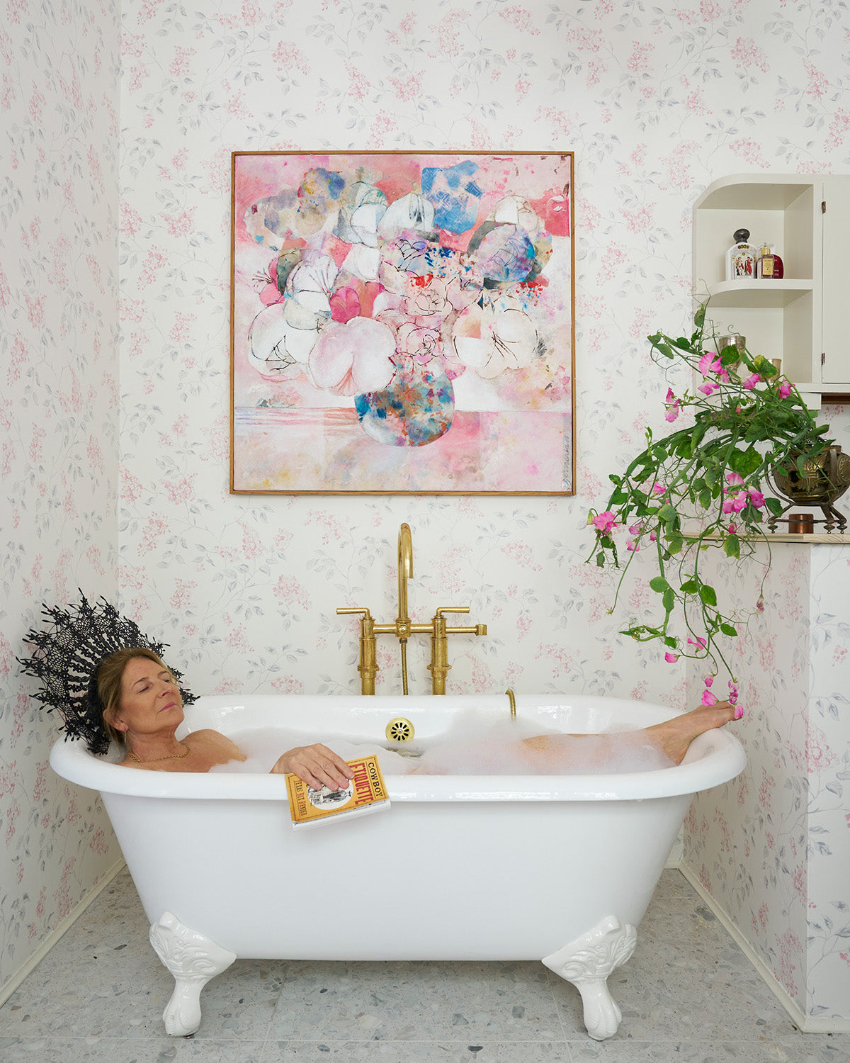 Kathryn M. Ireland soaks in a standing tub in the bathroom surrounded by Lilac Pink/Grey wallpaper.