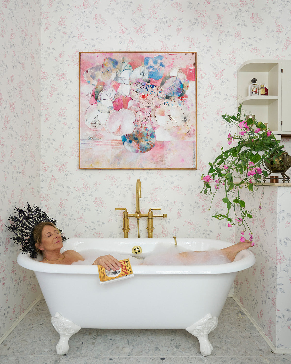 Kathryn M. Ireland soaks in a standing tub in the bathroom surrounded by Lilac Pink/Grey wallpaper.