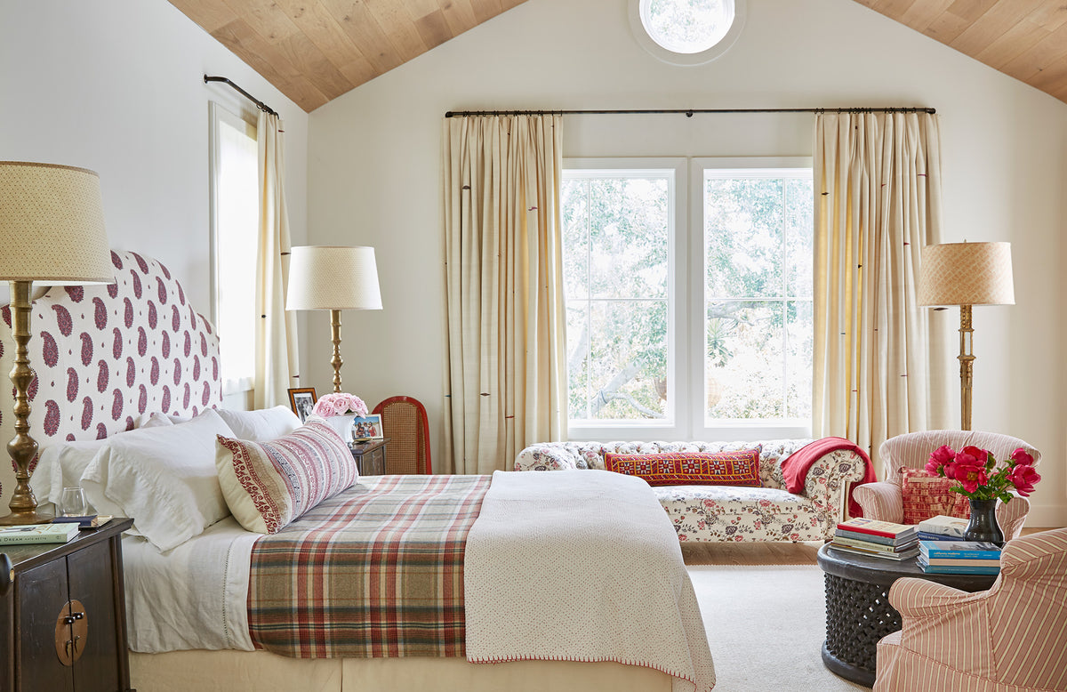 A beautifully styled bedroom interior featuring a bed with a Kirkbean Aubergine headboard, plaid bedding, and a Keltic Stripe Aubergine pillow designed by Kathryn M. Ireland