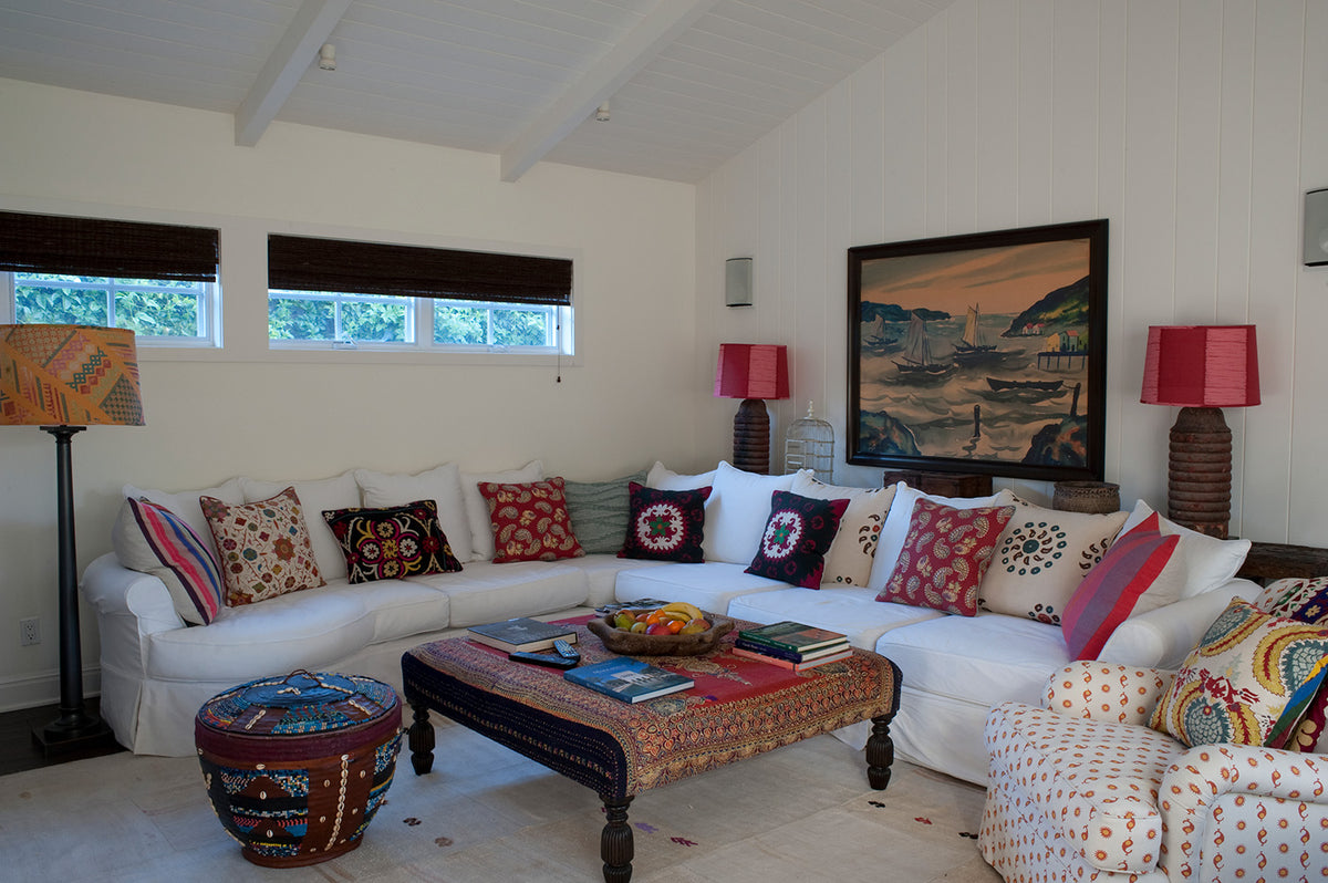 A styled living room featuring a white sectional sofa adorned with multiple colorful patterned throw pillows including in Marrakech Natural Teal, in Quilt Red, and in Safi Suzani Autumn, with an armchair in Casablanca Natural Natural/Flame & Mustard designed by Kathryn M. Ireland