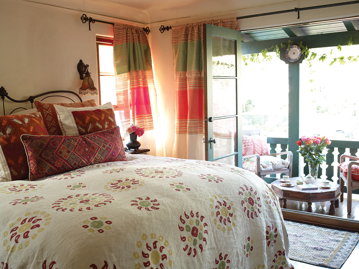 A cozy bedroom scene with a bed dressed in Natural Marrakech Natural/Cherry Red bedding designed by Kathryn M. Ireland
