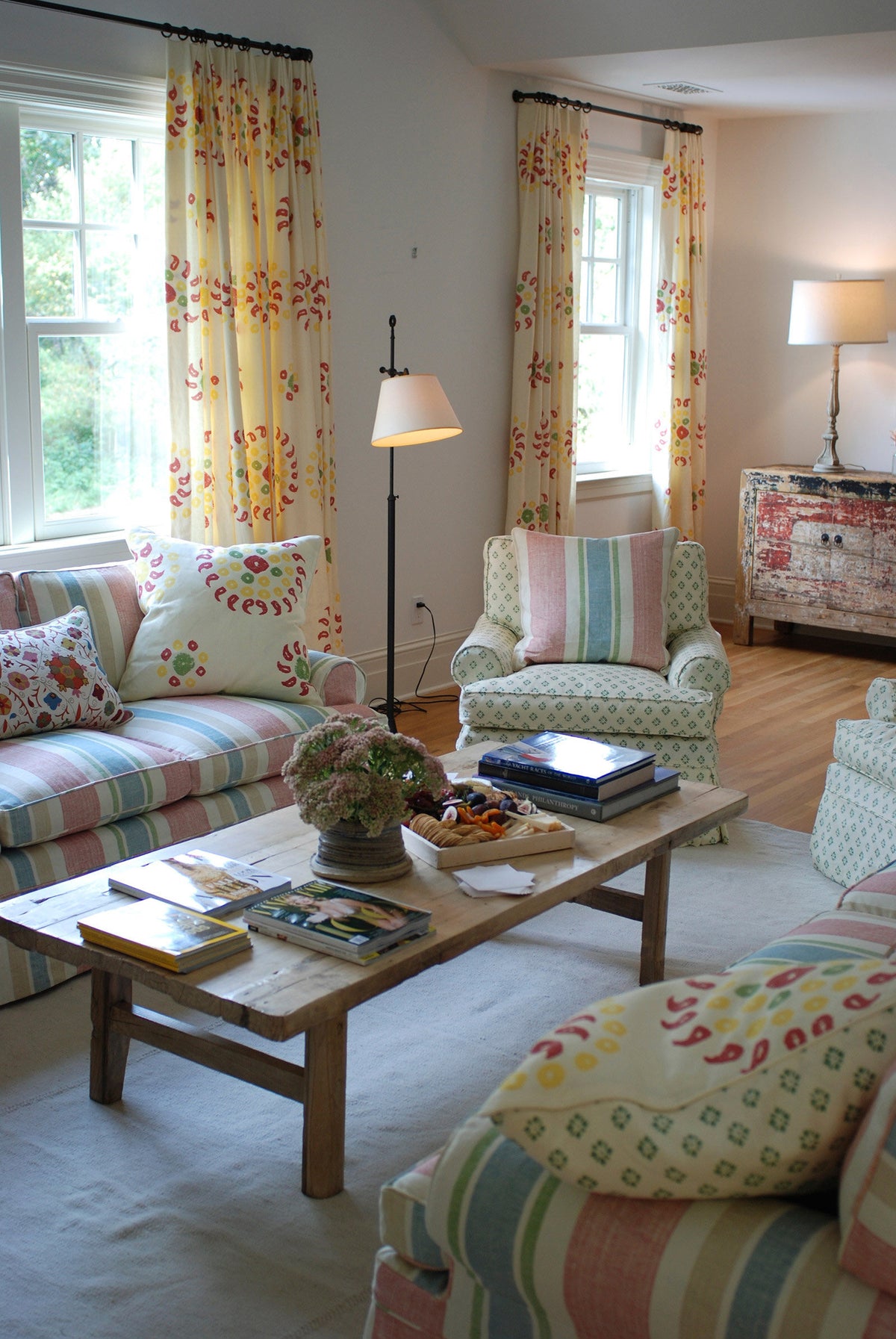 A living room with Natural Marrakech Natural/Cherry Red curtains and pillows, Sidone Pistachio Armchairs, and Moroccan Stripe sofas designed by Kathryn M. Ireland