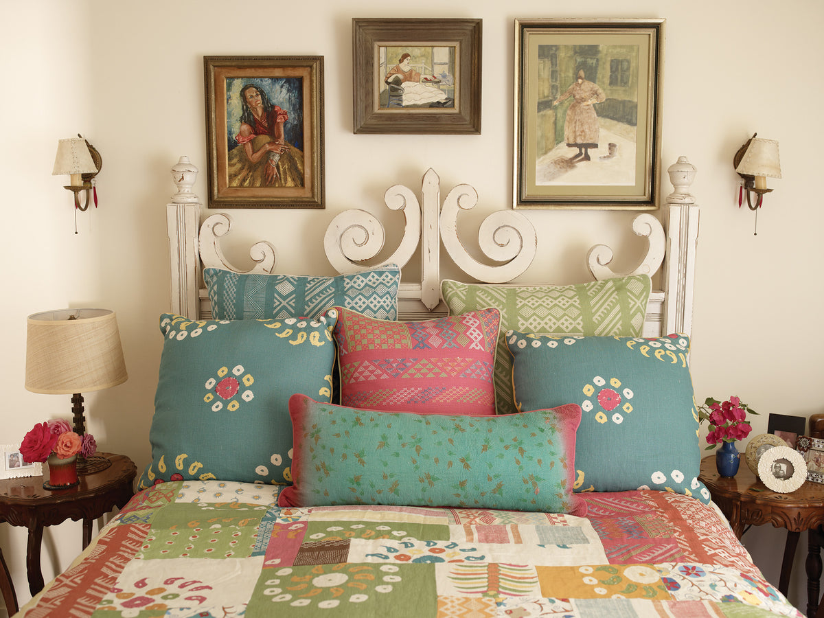 A bedroom featuring a Tangier Multi Peony Multi pillow, two Marrakech Teal pillows, a Tangier Natural Teal/Natural pillow, and a Tangier Natural Green/Natural pillow designed by Kathryn M. Ireland