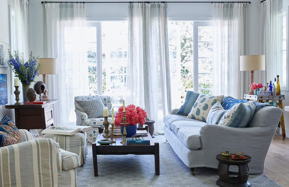 A bright, modern living room featuring a sofa, Moroccan Stripe Sky Blue armchair and ottoman, Safi Suzani Sky Blue armchair and pillow, and a Kirkbean Turquoise (Blue) pillow designed by Kathryn M. Ireland