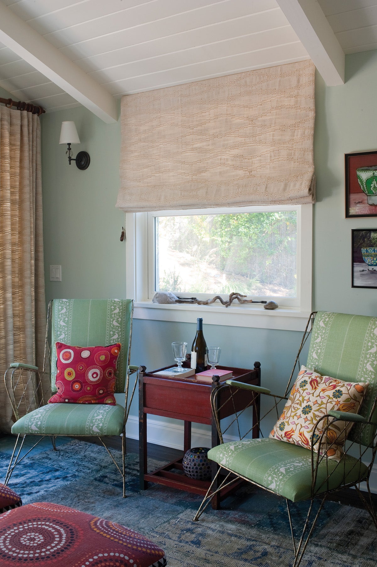 A styled interior room scene with two green upholstered armchairs, a window with a Moroccan Weave Natural roller blind and curtains, blue patterned rug, and decorative pillows designed by Kathryn M. Ireland