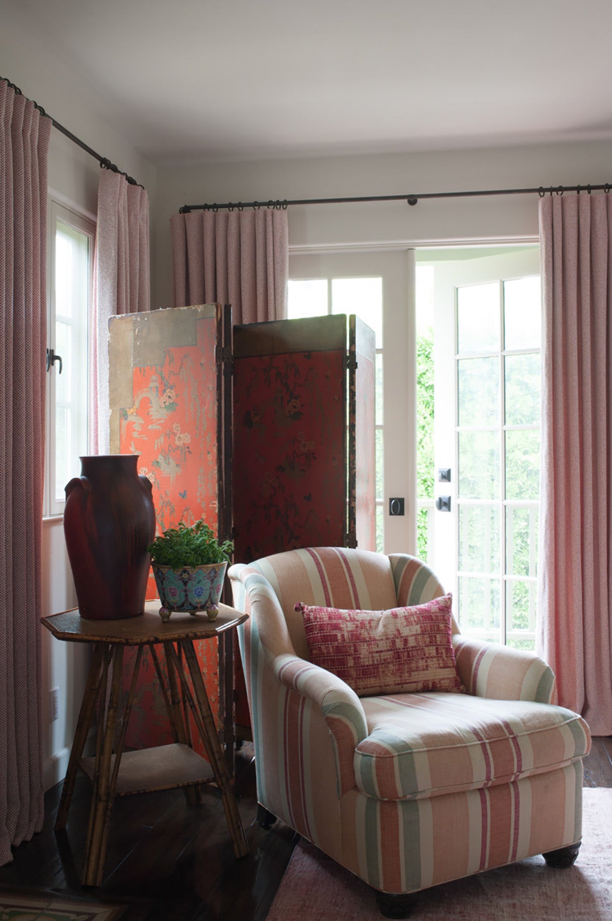 A cozy interior scene featuring a Morrocan Stripe Downtown on Champaign armchair with a pink patterned throw pillow, designed by Kathryn M. Ireland