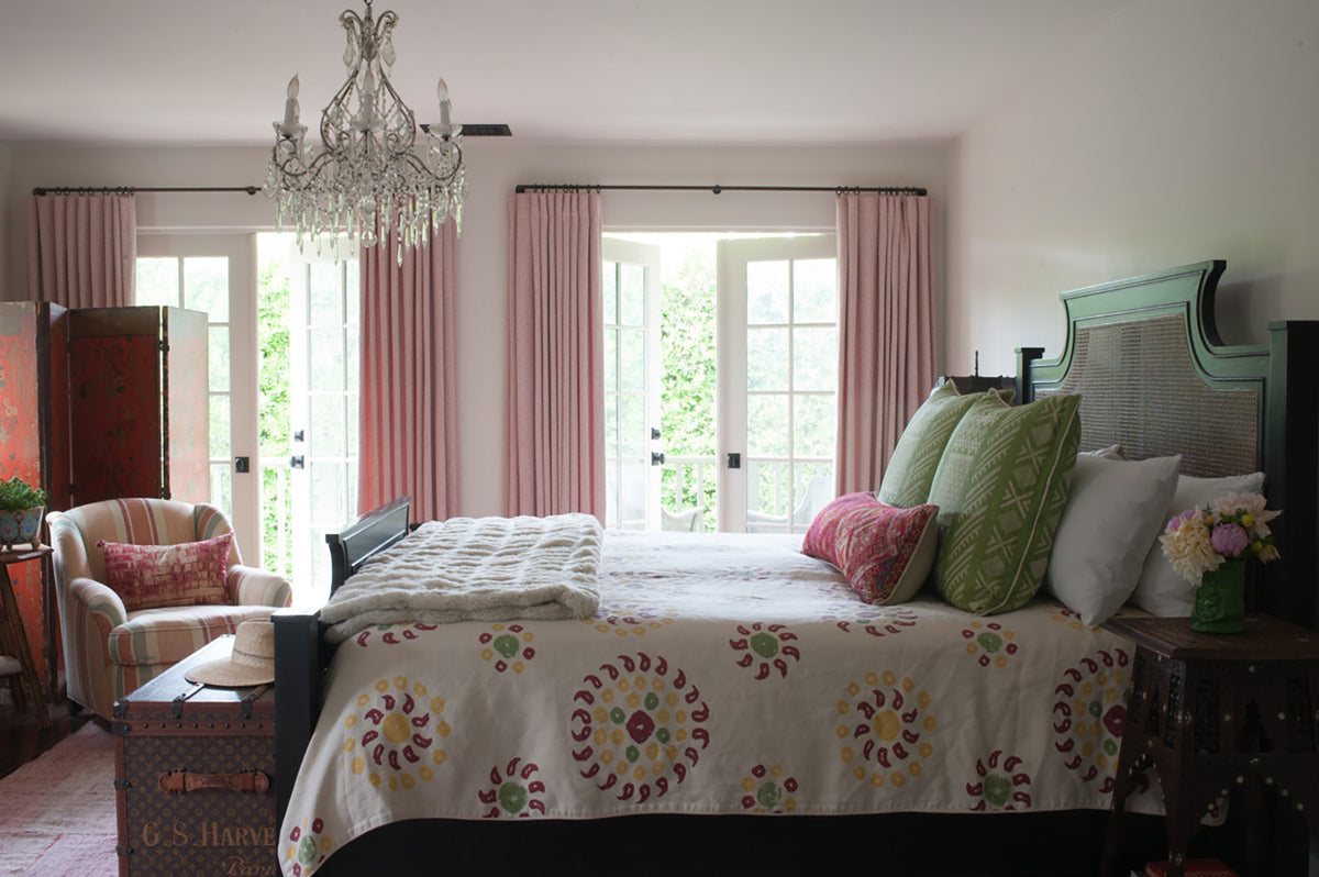 A styled bedroom interior featuring a bed dressed in a Marrakesh Natural Cherry Red bedding and Tangier Natural Margarita Green pillows, with an armchair in Moroccan Stripe Downtown on Champagne, designed by Kathryn M. Ireland