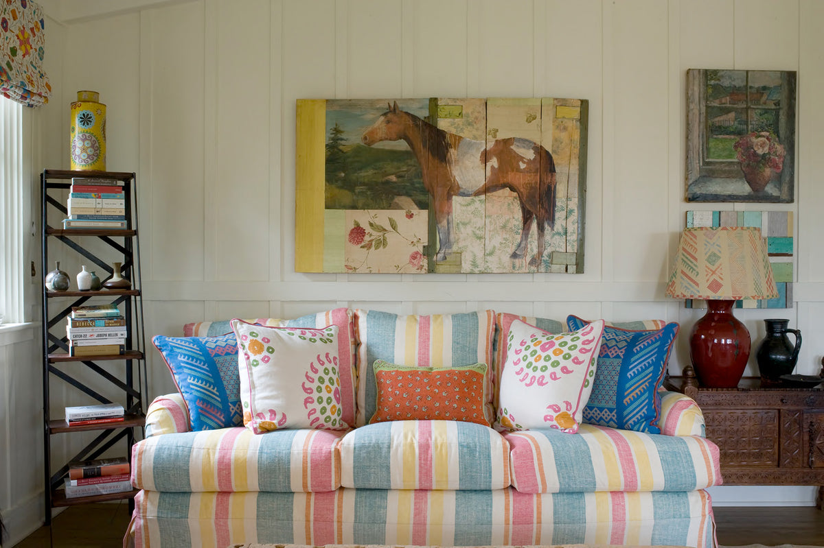 A sitting room featuring a Moroccan Stripes sofa, two pillows in Natural Marrakech Natural/Bubblegum Pink, two pillows in Tangier Multi Brilliant Blue Multi, and a lamp in Tangier Multi Sunburst/Multi designed by Kathryn M. Ireland.
