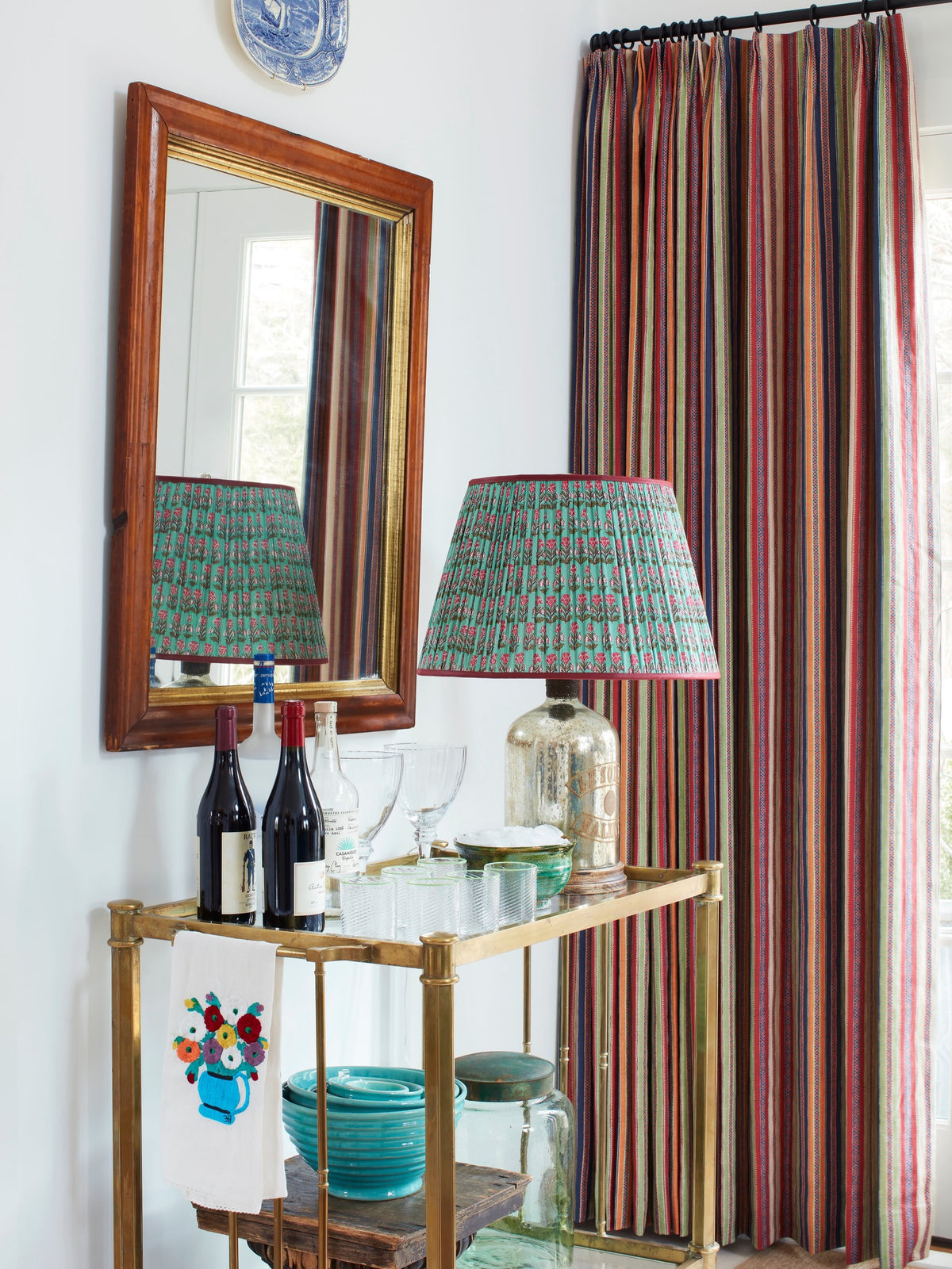 A bar cart in front of curtains in Ottoman Stripe Royal Multi, designed by Kathryn M. Ireland