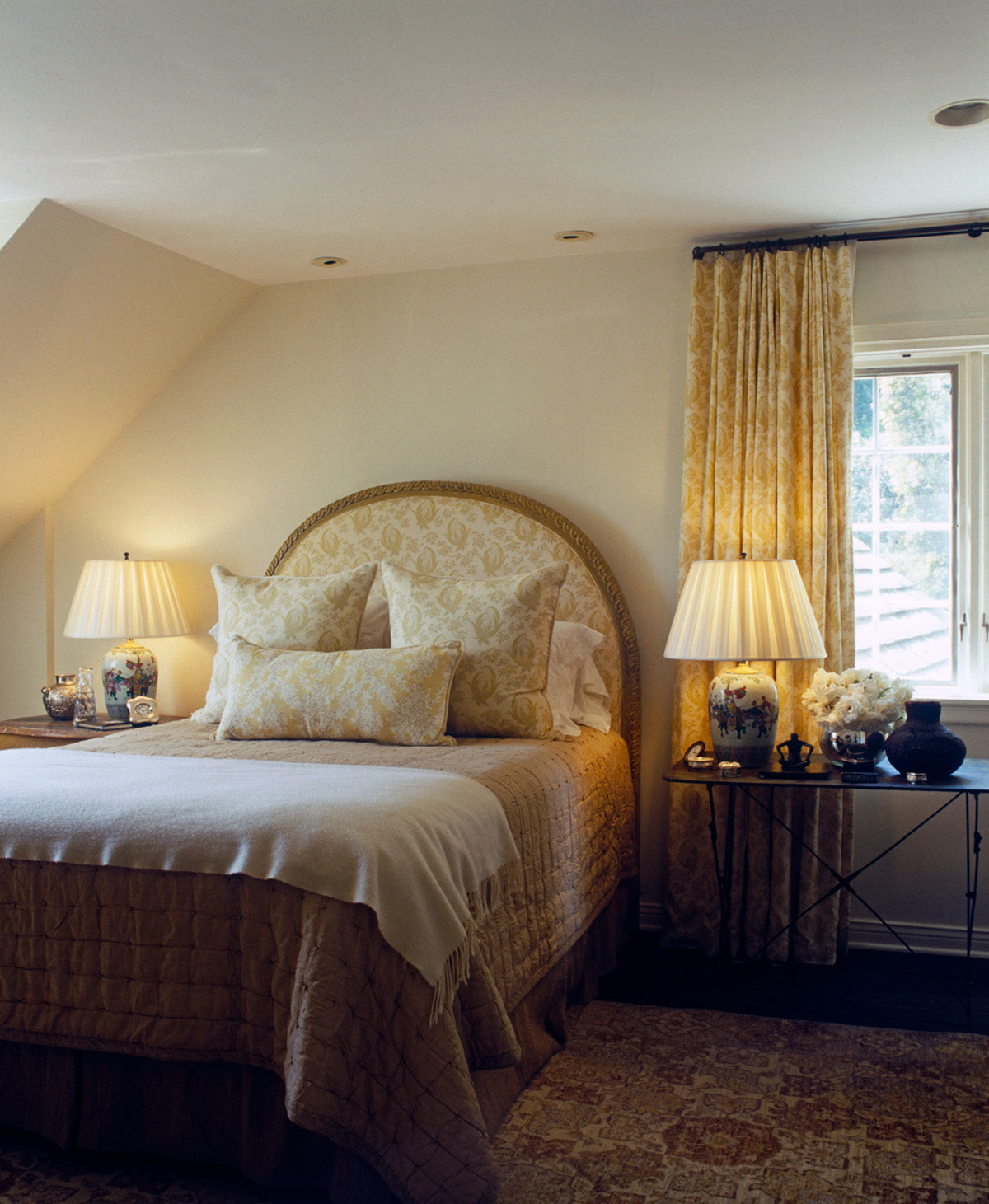 A styled bedroom interior featuring a bed with Paisley Stripe Red bedding and matching upholstered headboard, and a pillow and matching curtains in Ikat Yellow designed by Kathryn M. Ireland
