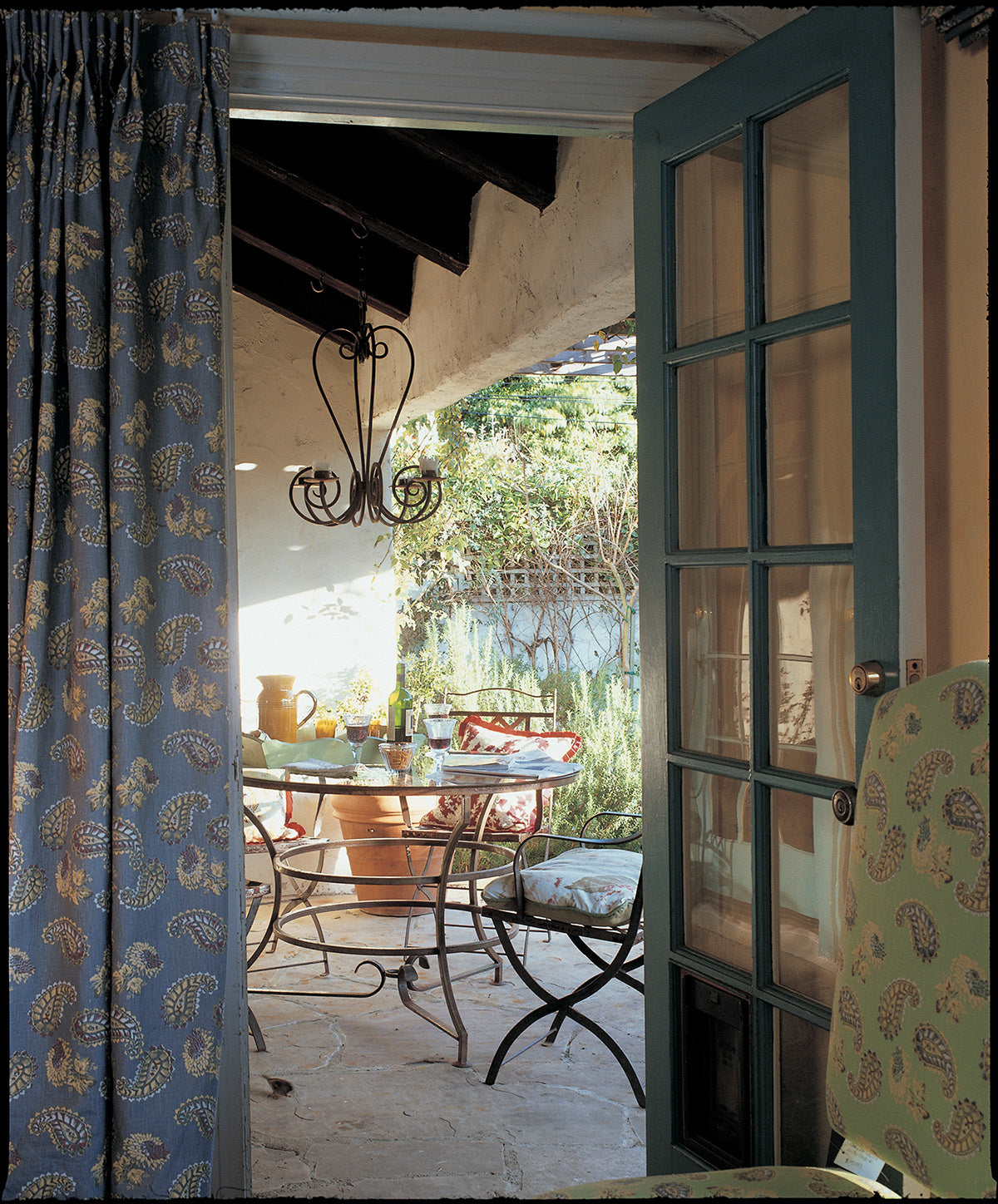 An interior doorway looking out onto a sunlit patio flanked by Quilt Blue curtain designed by Kathryn M. Ireland.