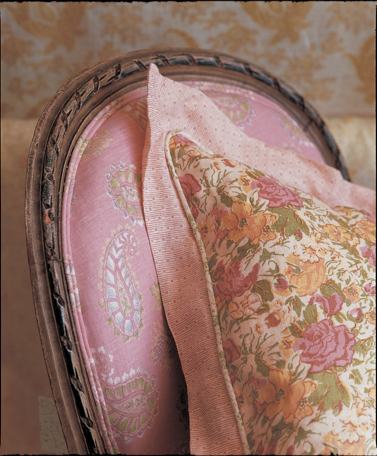A close-up of upholstered furniture showing a Quilt Pink fabric cushion, and and a floral throw pillow with Tonal Ticking Pink border designed by Kathryn M. Ireland