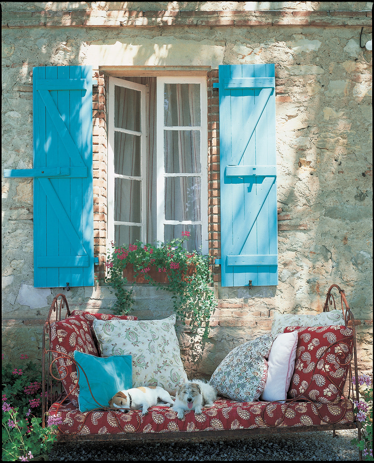 A rustic outdoor daybed with Quilt Red fabric and Paisley Stripe Red pillows designed by Kathryn M. Ireland