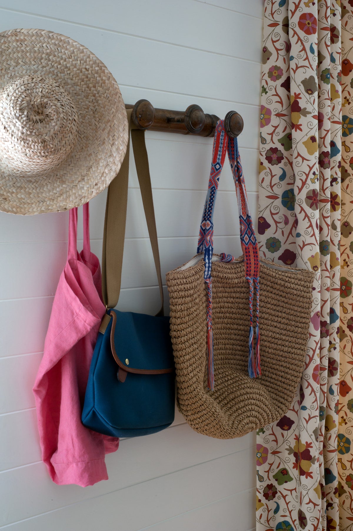 A straw hat hangs on a wooden wall rack next to a Safi Suzani Autumn curtain designed by Kathryn M. Ireland