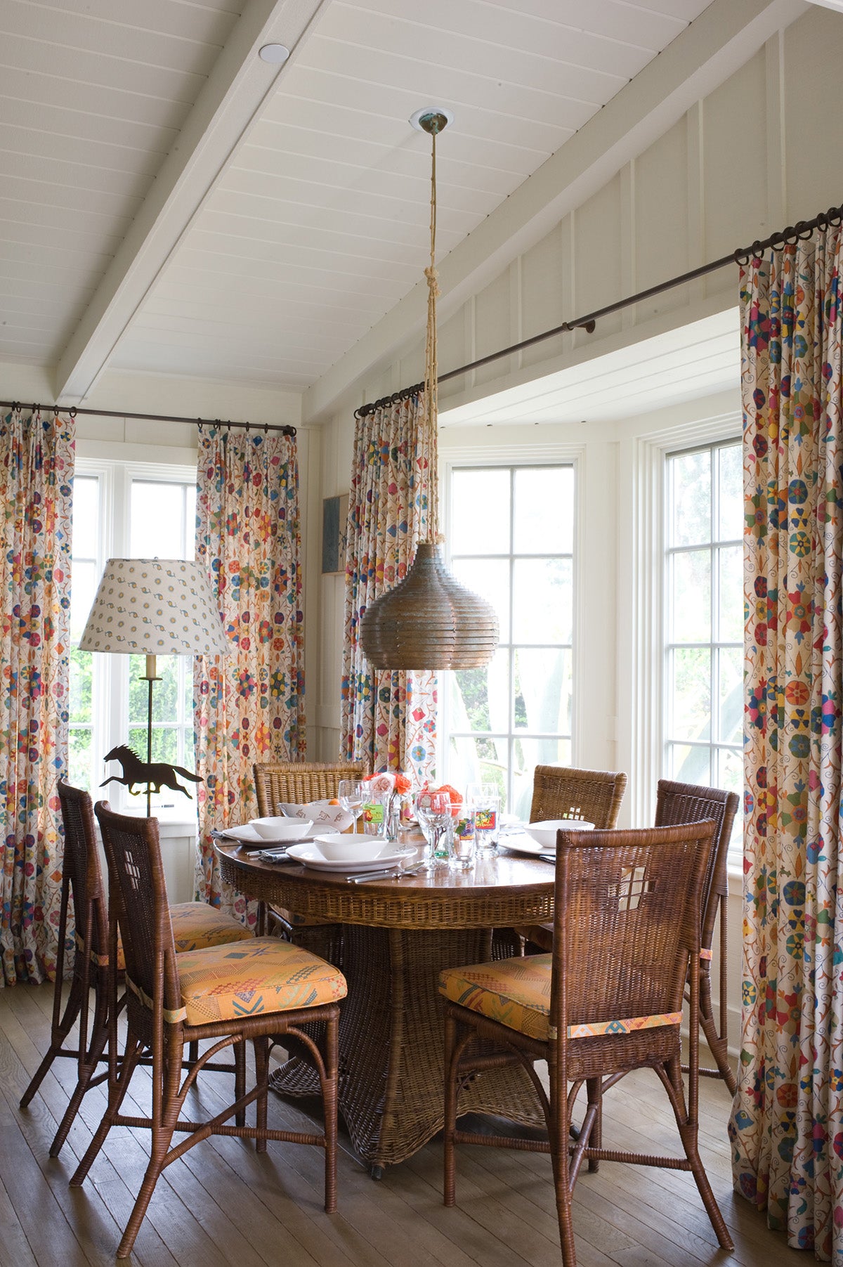 A dining room interior with a round wicker dining table, and Safi Suzani Fiesta curtains designed by Kathryn M. Ireland
