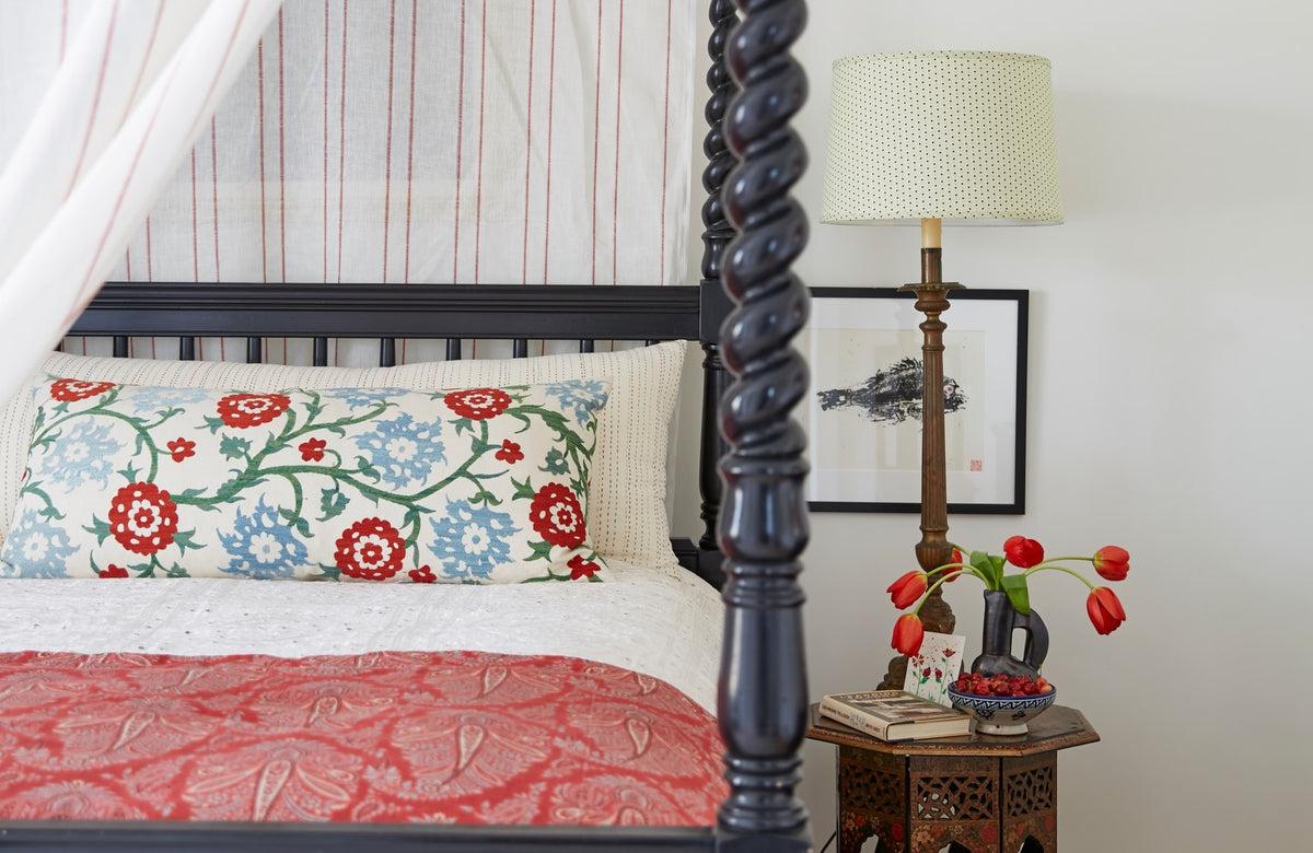 A four-coaster bed featuring Sheer Stripe Red bed curtains, a comforter in Egerton Paisley Red, and a long lumbar pillow in Hand-Stitched Multi fabric, designed by Kathryn M. Ireland