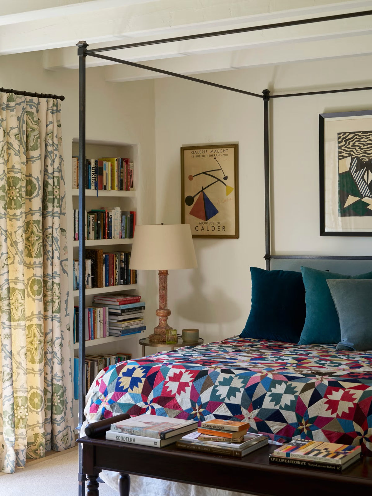 A styled bedroom interior featuring a four-poster frame bed with a colorful geometric quilt and curtains in Sultan Suzani Sea, designed by Kathryn M. Ireland.