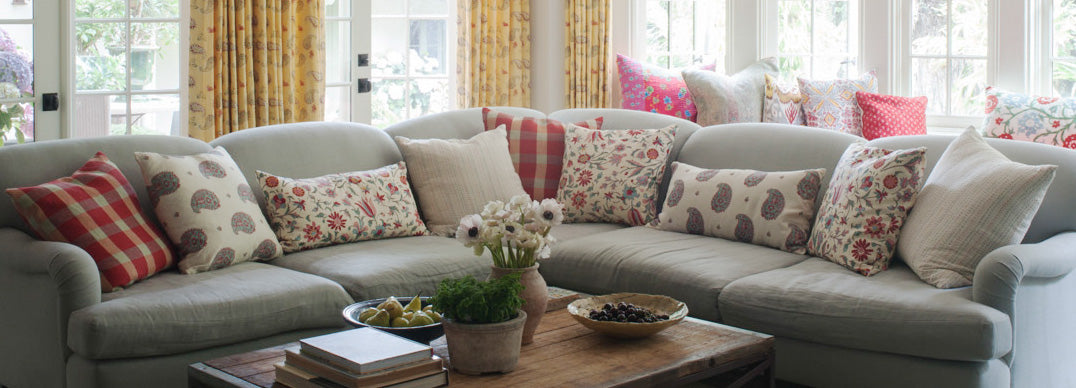 A gray upholstered couch featuring pillows in Tatiana Red/Pink/Blue and Kirkbean Red (Turquoise) designed by Kathryn M. Ireland