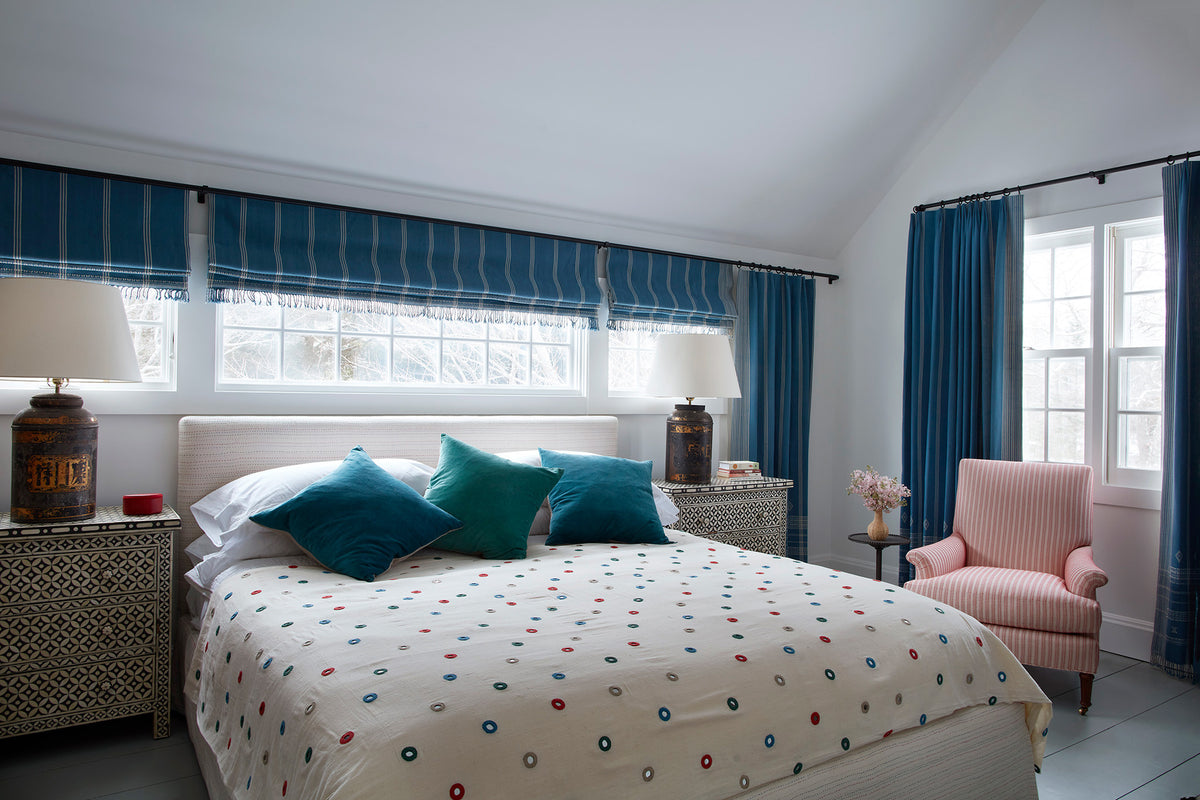 A bedroom with Indian Mirror Multi bedspread and Zig Zag Red arm chair.