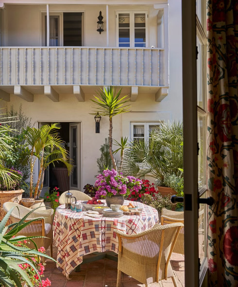 An outdoor dining area on a sunlit patio with a round table covered in a tablecloth in Togo Check Multi, designed by Kathryn M. Ireland. 